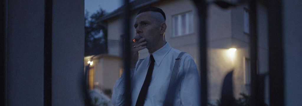 Christian Friedel dans le rôle de Rudolf Höss fume un cigare à la nuit tombée.